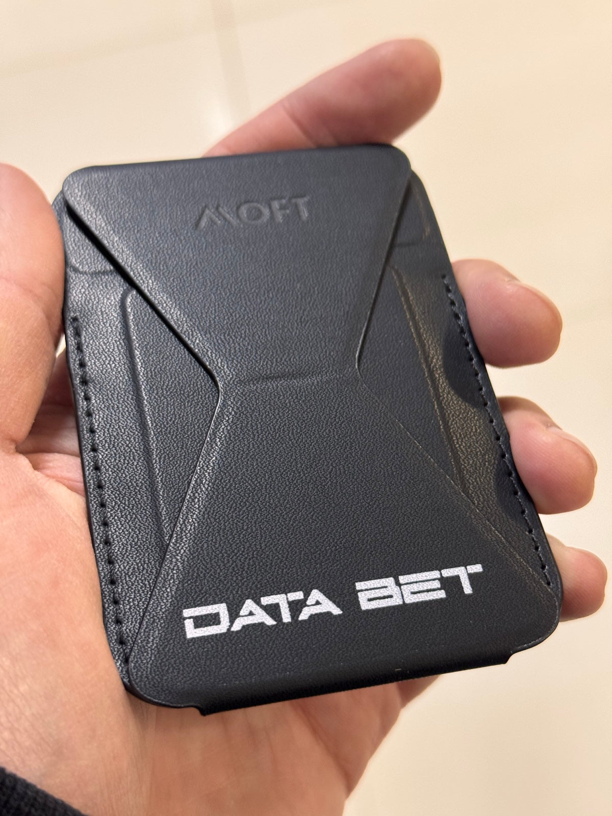 Гаманець-підставка MOFT з білим логотипом DATA BET у руці